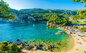 Une plage côtière aux eaux turquoise et limpides, avec un rivage rocheux et un petit bateau.