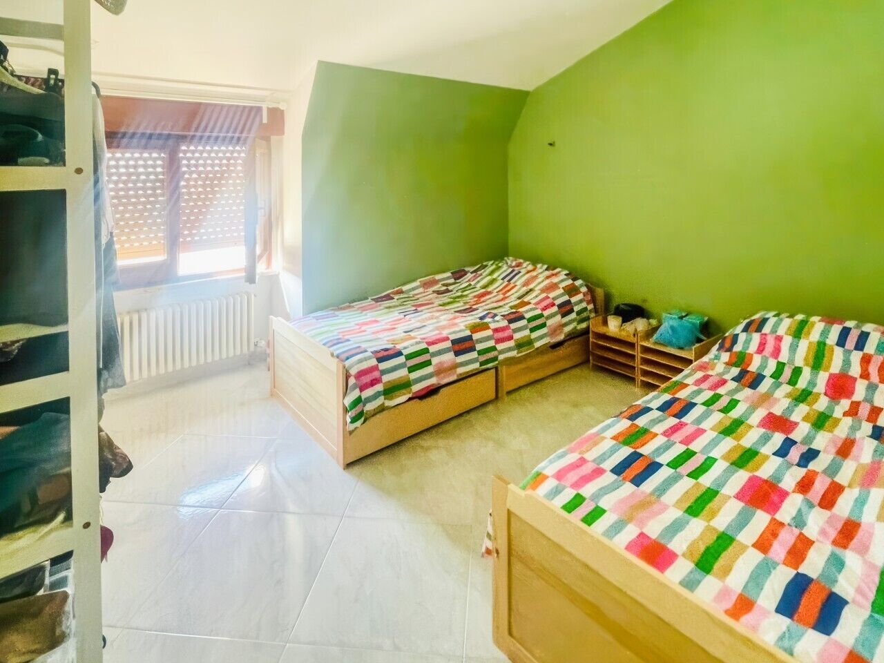 Une chambre avec deux lits, un radiateur, une fenêtre et une armoire en bois.
