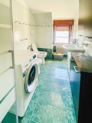 A compact bathroom with a washing machine, toilet, and sink. - The Sabi Terraces (Giulianova)