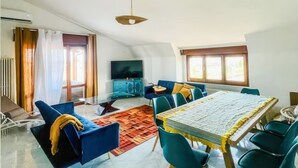 Ein großzügiger Wohnbereich mit Esstisch, blauen Sofas und einem Fernseher im Hintergrund.