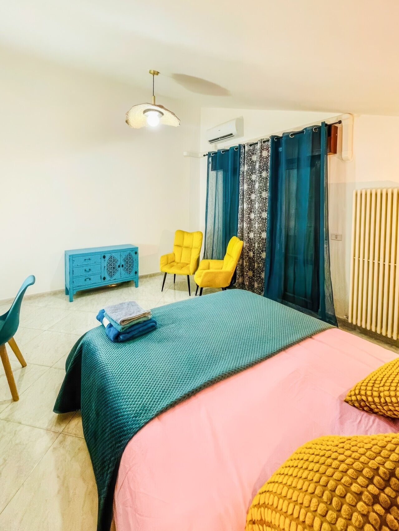 A bedroom with a bed, two chairs, a blue dresser, a ceiling fan, and an air conditioning unit.