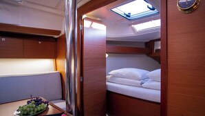 Una cabina compatta e ben illuminata con un letto, un tavolino con una ciotola di frutta e un lucernario sopra il letto.
