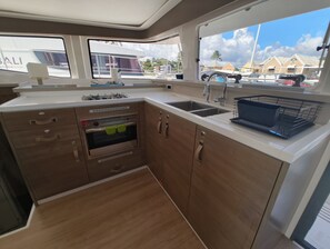 A compact kitchen with a built-in oven, a sink, and a window overlooking a marina. - Caribbean Dream: Sun-Kissed Sailing Adventure from Guadalupe, Grande-Terre (Pointe-à-Pitre)