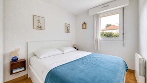 Una camera da letto con un letto, pareti bianche, una finestra con tende e un termosifone.