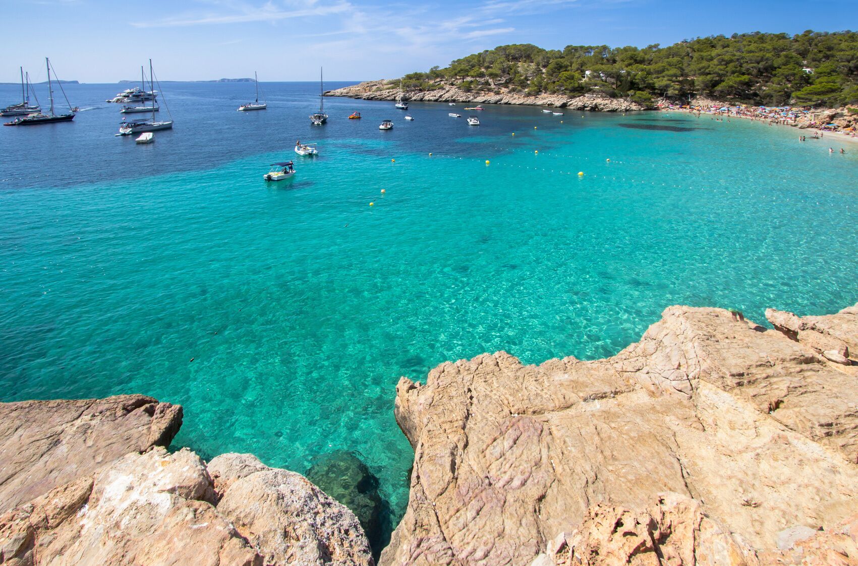 Zona costera con aguas turquesas cristalinas, costas rocosas y barcos.