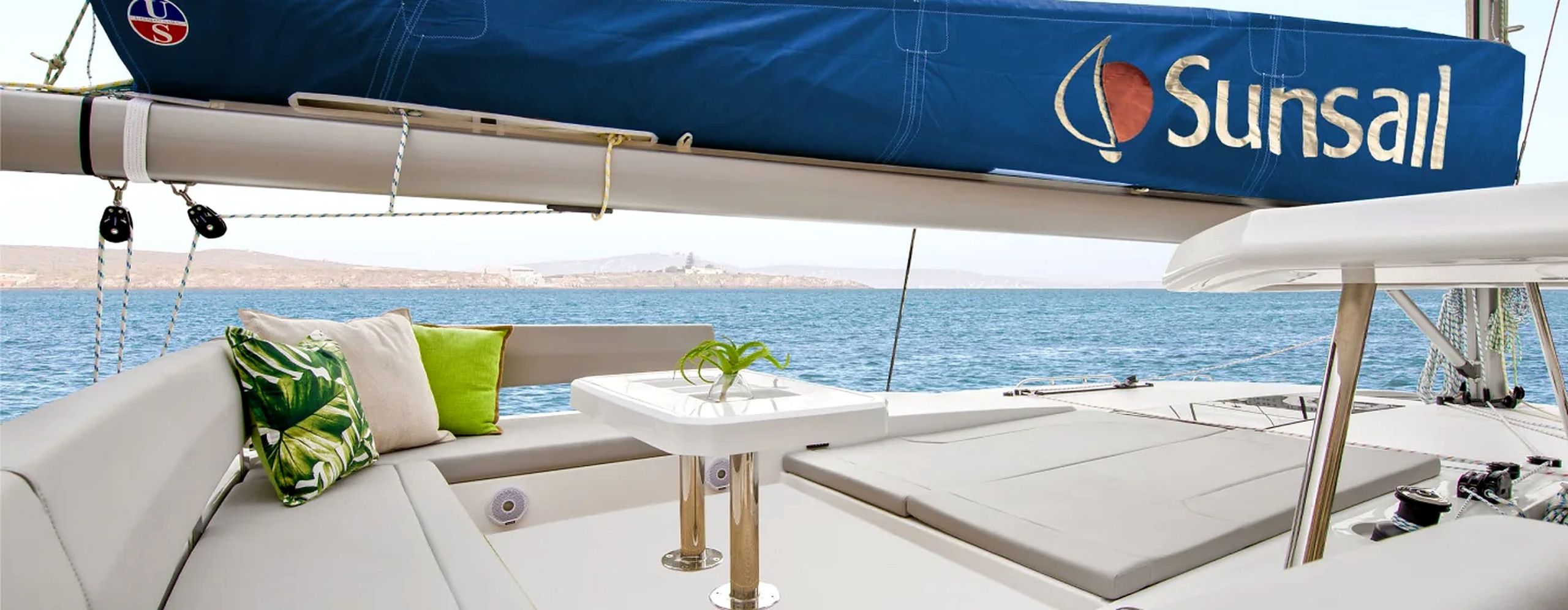 A yacht interior with a covered area, cushions, a small table, and a view of the sea.