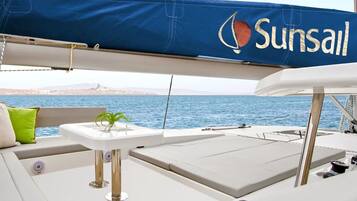 A yacht interior with a covered area, cushions, a small table, and a view of the sea.