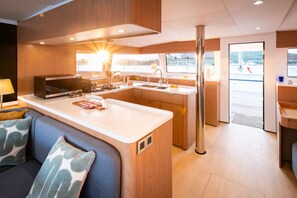 A modern kitchen with a central island, a dining area with a sofa, and a view of the outdoors. - Sun-Kissed Sailing Adventure in Islas Baleares, Mallorca (Andratx)