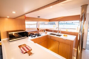 A compact kitchen with a microwave, stove, sink, and wooden cabinets. - Sun-Kissed Sailing Adventure in Islas Baleares, Mallorca (Andratx)