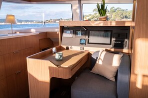 A boat's interior with a wooden desk, a cushioned seat, a control panel, and a potted plant. - Sun-Kissed Sailing Adventure in Islas Baleares, Mallorca (Andratx)
