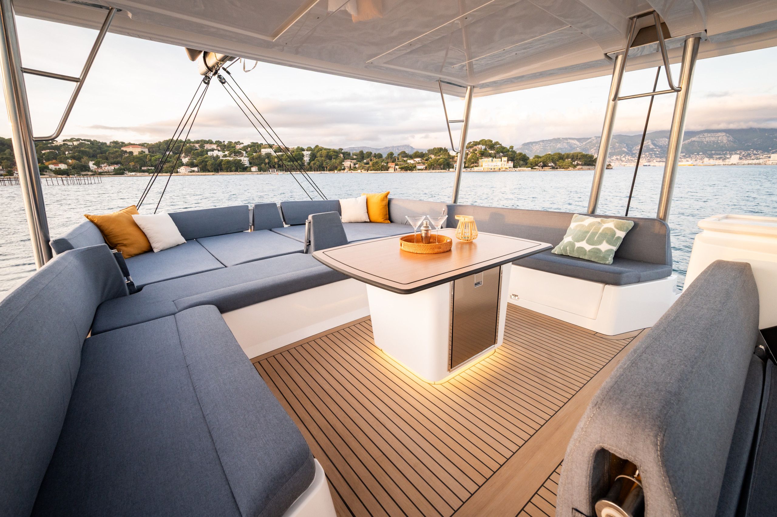 A boat's deck with a seating area, a table, and a view of the water and land.