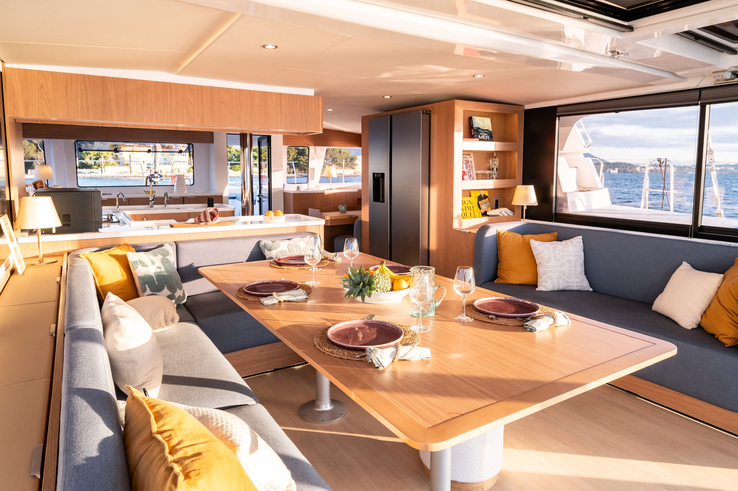 A yacht interior with a dining area, seating, and a view of the sea.