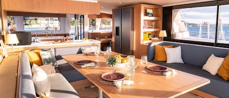 A yacht interior with a dining area, seating, and a view of the sea.