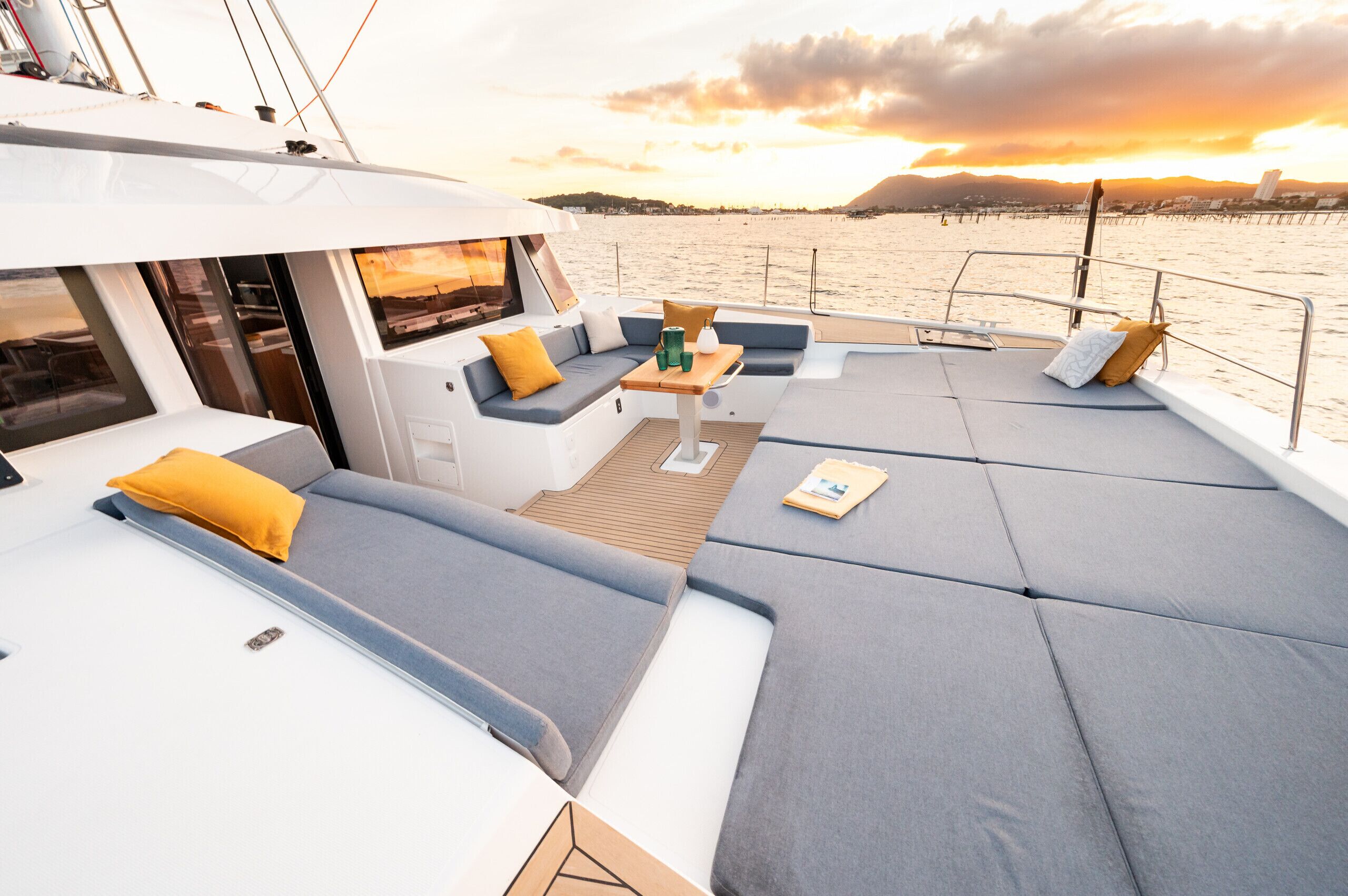 Il ponte di uno yacht con zone relax, un tavolo e vista sull'acqua e sulla costa in lontananza.