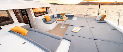 Il ponte di uno yacht con zone relax, un tavolo e vista sull'acqua e sulla costa in lontananza.