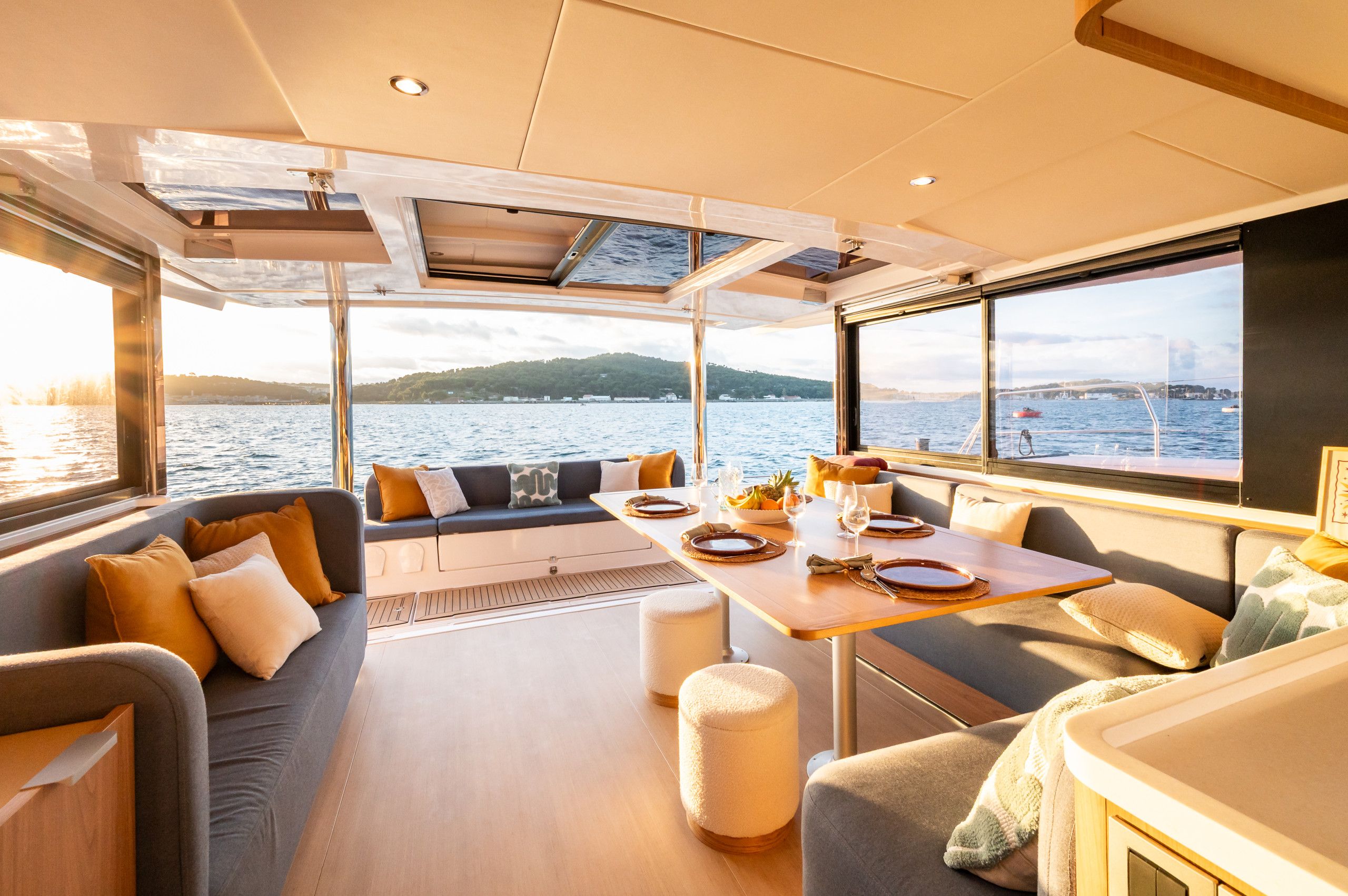 Interior de un yate con comedor, asientos y vista al agua.