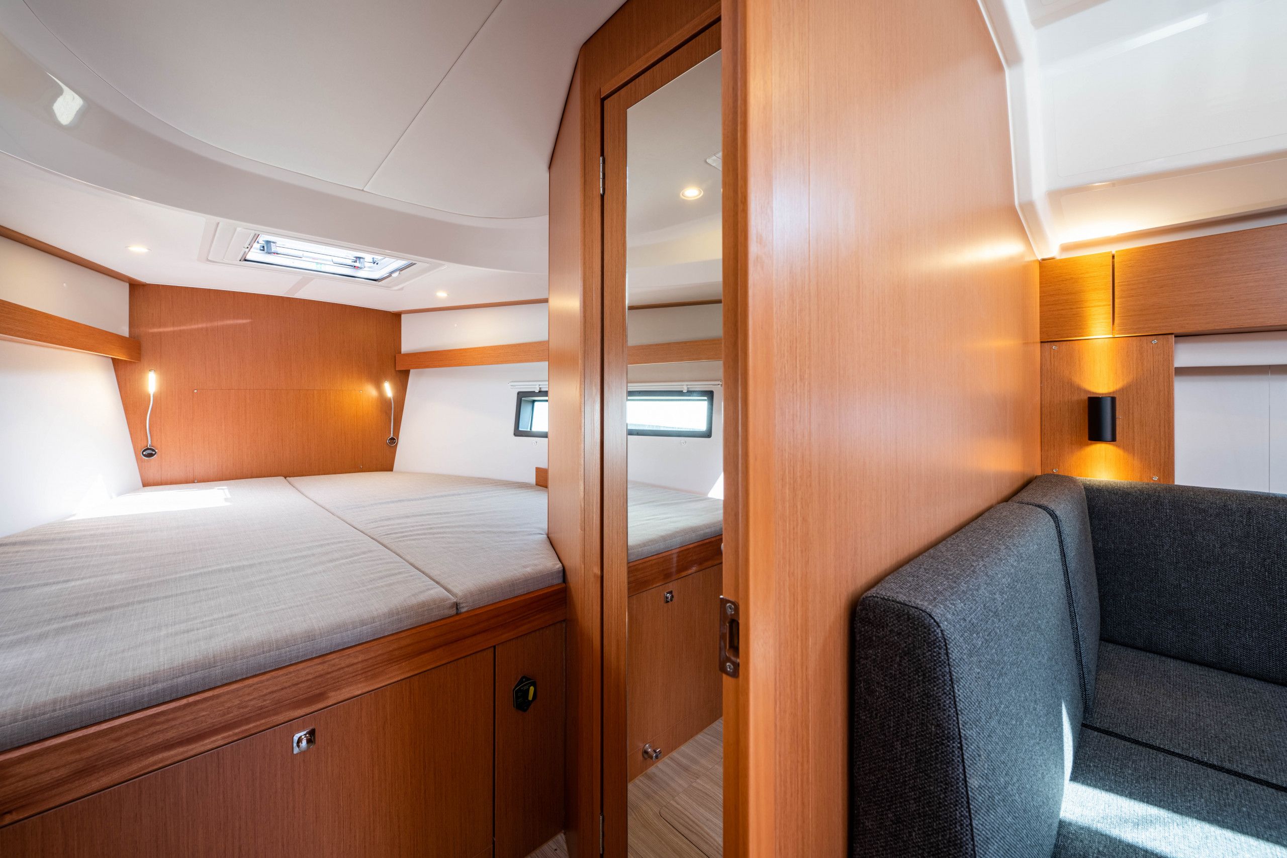 A compact interior with a bed, a sofa, a mirror, and a small window.