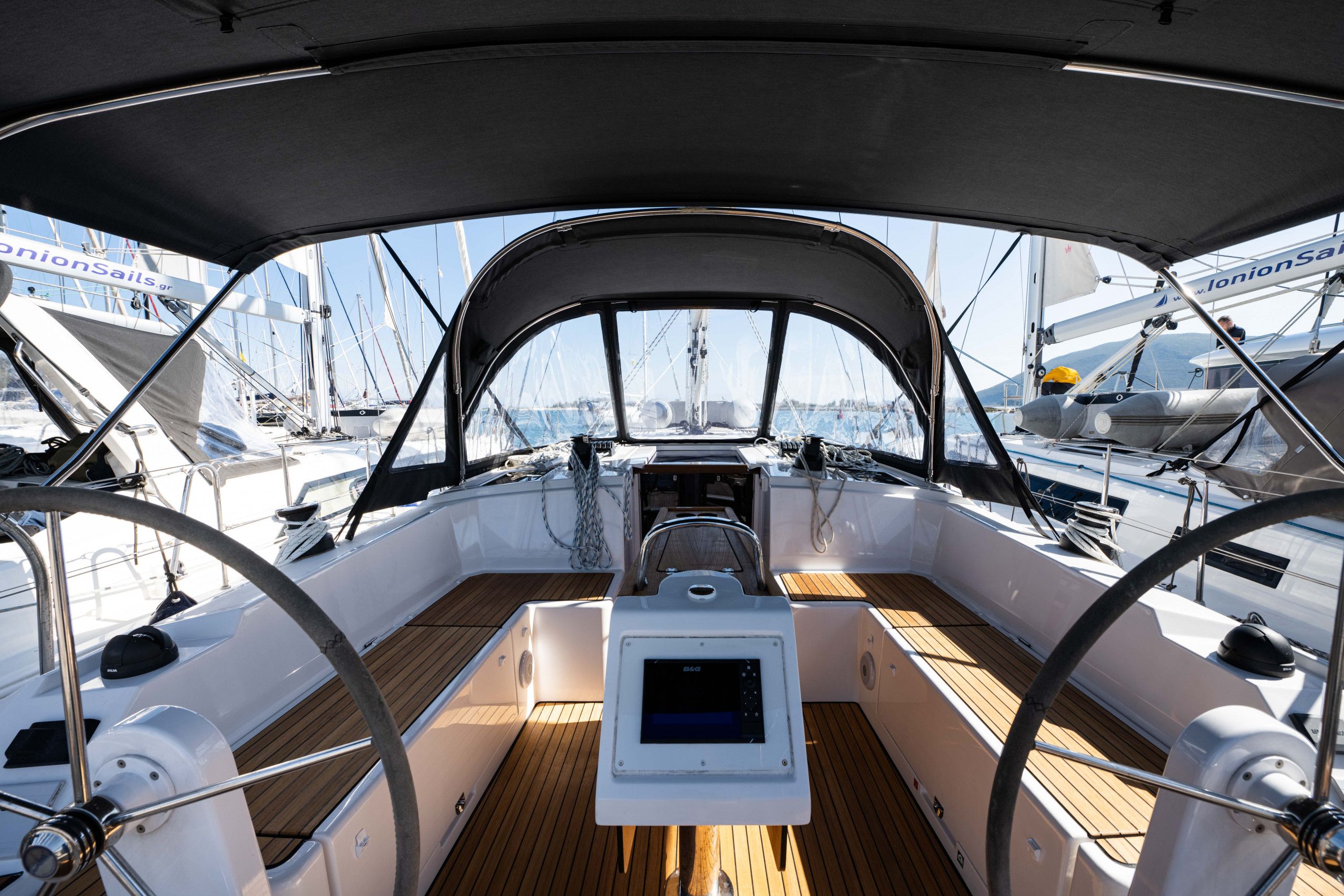Ein Bootsdeck mit einer zentralen Steuerung, Holzboden und mehreren Segelbooten im Hintergrund.