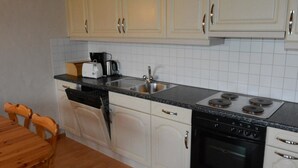 Une cuisine avec des meubles blancs, une cuisinière noire et une machine à café.