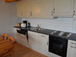A kitchen with white cabinets, a black stove, and a coffee maker. - Anne (2. Stock) Appartement/Fewo, Dusche oder Bad, WC 12-Bettwohnung by Interhome (Gstaad)