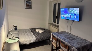Un dormitorio con cama, mesita de noche, lámpara, televisor y ventana.