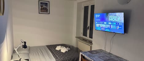 A bedroom with a bed, bedside table, lamp, TV, and a window.