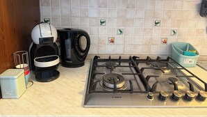 Una cocina con estufa a gas Bosch, una cafetera Krups, una jarra de café negra y un cubo de basura color turquesa.