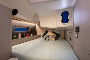 Ein gemütliches, gut beleuchtetes Schlafzimmer mit einem Bett, Kissen, einer kleinen Ablagefläche mit Gegenständen, einem Fenster und einem Bedienfeld.