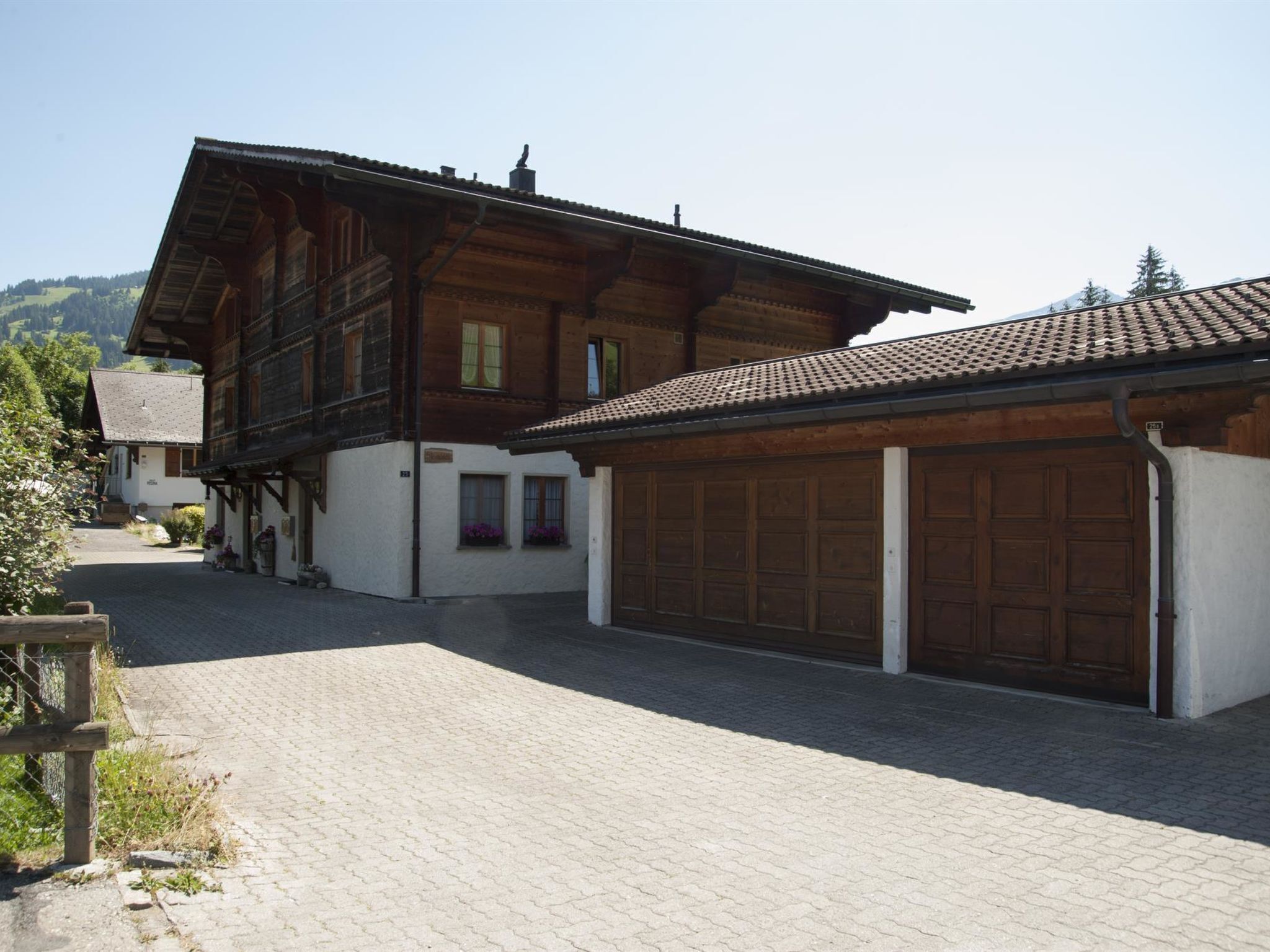 Un edificio in legno tradizionale con garage, vialetto lastricato e montagne sullo sfondo.