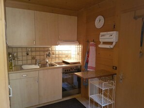 Eine kleine Küche mit Spüle, Herd und Backofen, Holzschränken und einer Wanduhr.