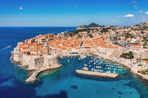 Una ciudad costera con arquitectura histórica, un puerto lleno de barcos y un mar azul y transparente.