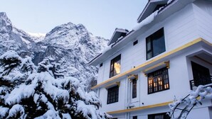A white building with multiple windows and balconies, surrounded by snow-covered trees and mountains. - Mystique Valley by Trekocity  (Lachung)