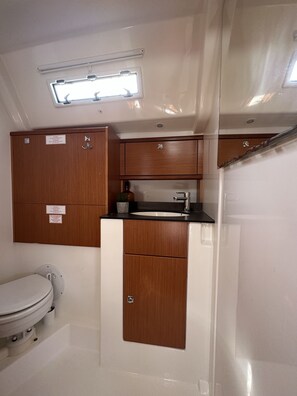 A compact bathroom with a toilet, a sink, and wooden cabinets. - Sun-Kissed Sailing Adventure in Zadar, Croatia (Bibinje)