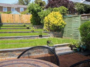 A patio area with a tiled table and chairs, a stone retaining wall, and a variety of potted plants. - The Dacha (Winchester)