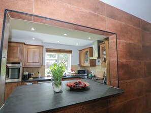 A kitchen with a large mirror, wooden cabinets, a black countertop, and a bowl of fruit. - The Dacha (Winchester)