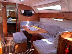 A compact interior with a sofa, a small table, a television mounted on the wall, and a window providing natural light. - Sun-Kissed Sailing Adventure in Northern Croatia (Punat)