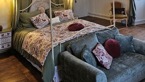 A four-poster bed with a canopy, a chandelier, a green sofa, and a wooden floor.