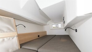 Habitación compacta y moderna con cama, una ventana pequeña y una lámpara fijada a la pared.