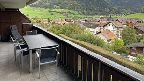 Ein Balkon mit Tisch und Stühlen mit Blick auf ein Dorf und Berge.