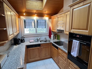 A kitchen with wooden cabinets, a granite countertop, a window with curtains, and a digital clock. - Hübeli (Streit) Appartement/Fewo, Dusche und Bad, WC 6-Bettwohnung by Interhome (Zweisimmen)