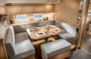 A modern interior with a dining area featuring a table set for two, cushioned seating, and a view through a window. - Sun-Kissed Sailing Adventure in Istria, Croatia (Pula)