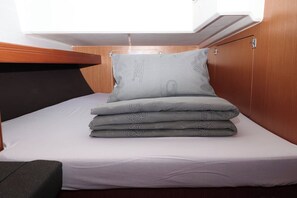 A compact bed with a grey pillow and folded blankets, a wooden headboard, and a small bench. - Sun-Kissed Sailing Adventure in Zadar, Croatia (Biograd na moru)