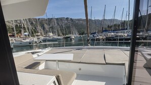 A boat deck with seating areas, a control panel, and a view of a marina with boats and mountains in the background. - Dubrovnik Delight: A Sun-Kissed Sailing Experience (Komolac)