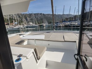 A boat deck with seating areas, a control panel, and a view of a marina with boats and mountains in the background. - Dubrovnik Delight: A Sun-Kissed Sailing Experience (Komolac)