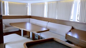 Ett kompakt inre utrymme i husbilen med en central sittgrupp, ett litet bord och ett fönster med gardiner.