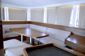 A compact RV interior with a central seating area, a small table, and a window with curtains. - Sun-Kissed Sailing Adventure in the Ionian Islands, Lefkada (Lefkada)