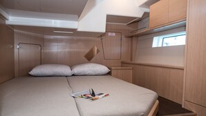 Quarto compacto de motorhome com cama, almofadas, uma revista e uma janela.