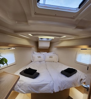 A compact bedroom with a bunk bed, a skylight, a small table, and a potted plant.