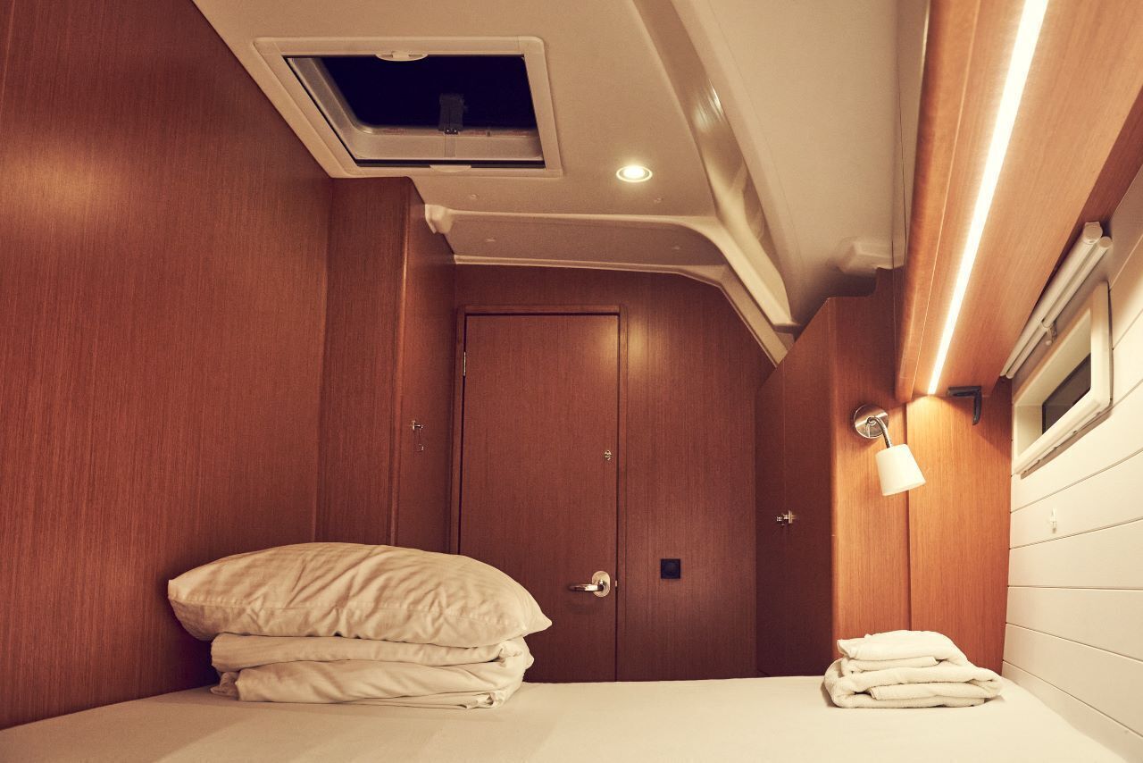 Une petite cabine bien aménagée et bien éclairée, avec un lit, une petite fenêtre et un luminaire fixé au mur.