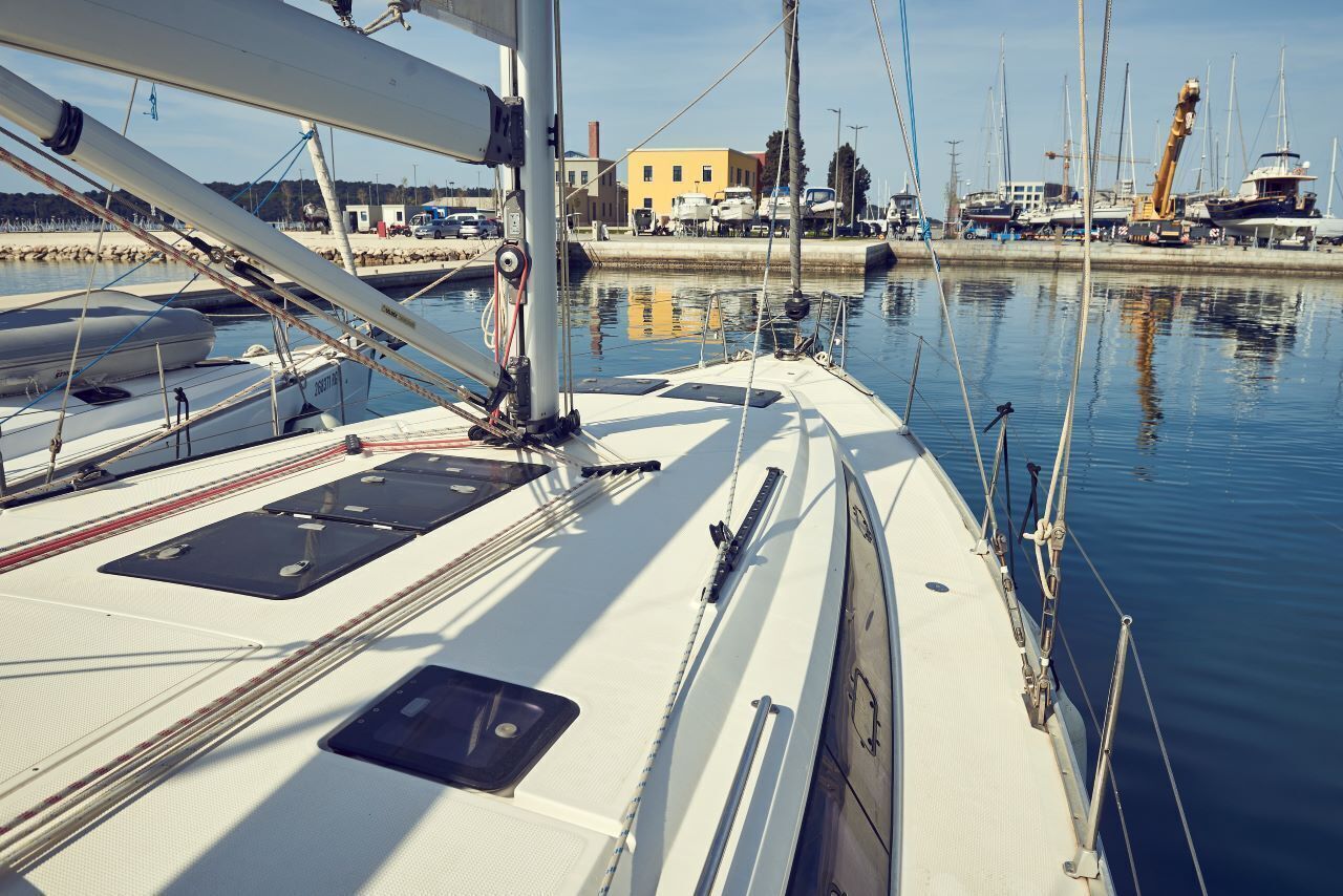 A marina with multiple sailboats docked, a building in the background, and calm water.